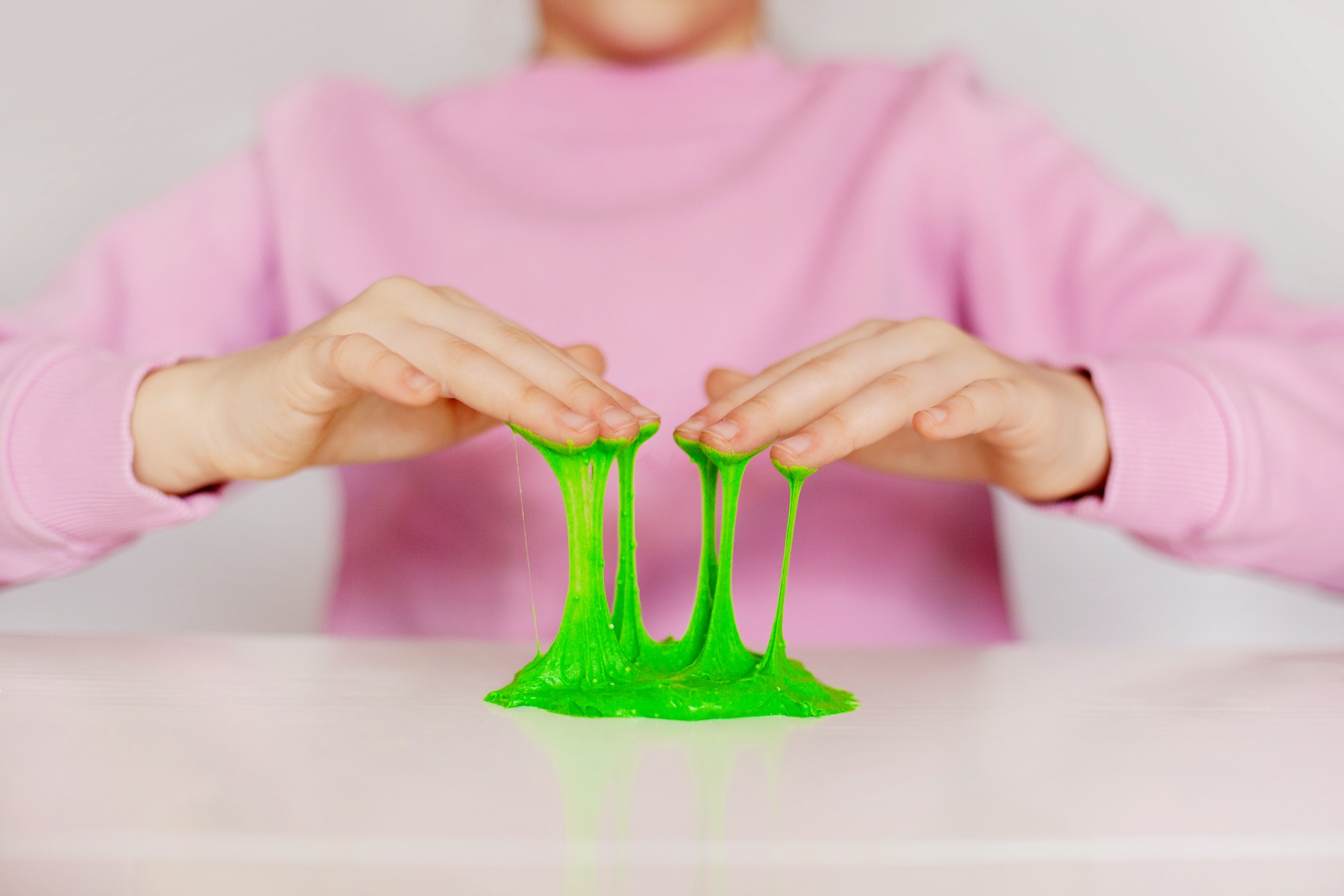 Hands hold a homemade toy called slime. A child plays with green sticky slime